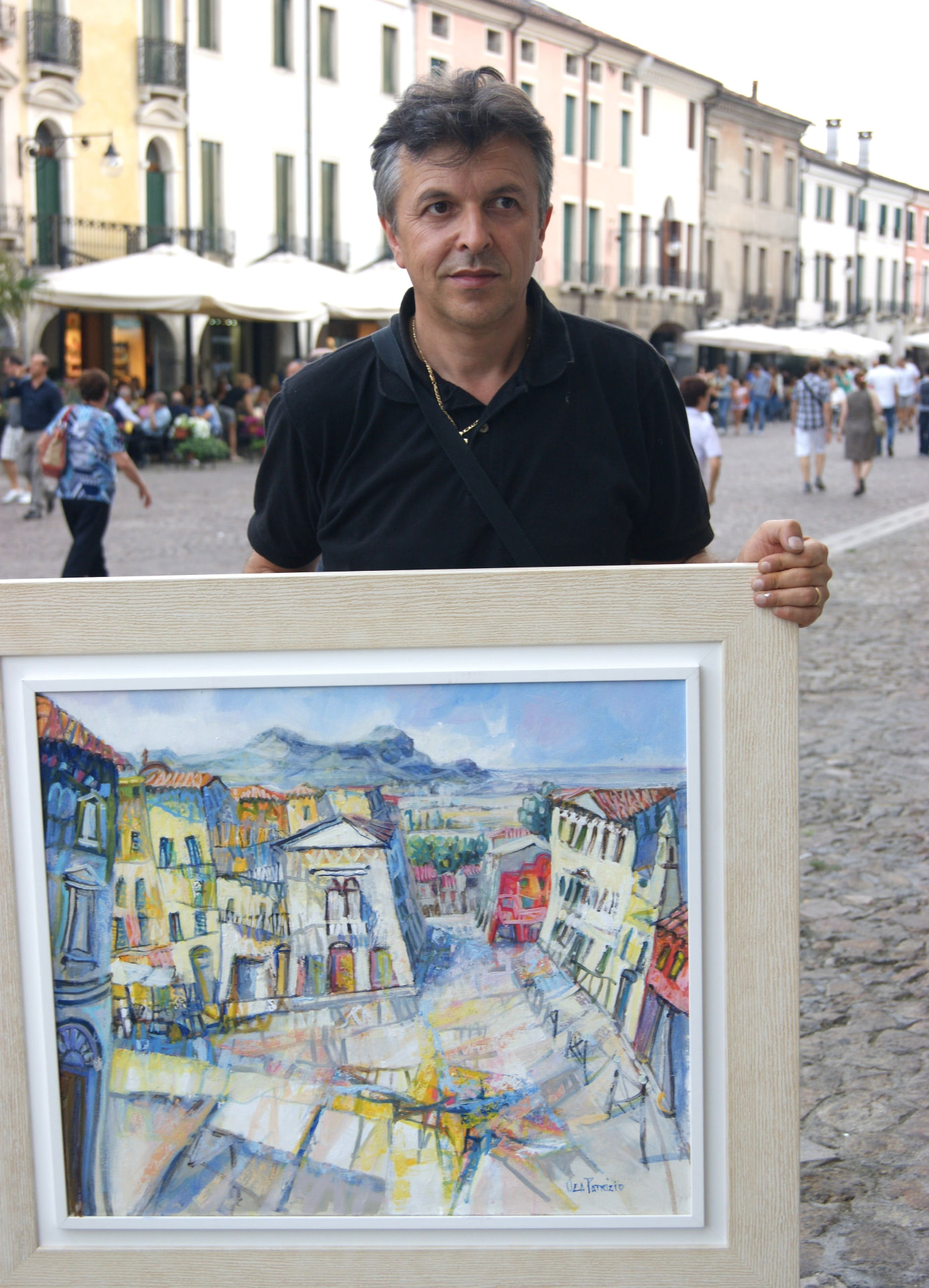Patrizio Oca mostra un dipinto incorniciato nella piazza del borgo