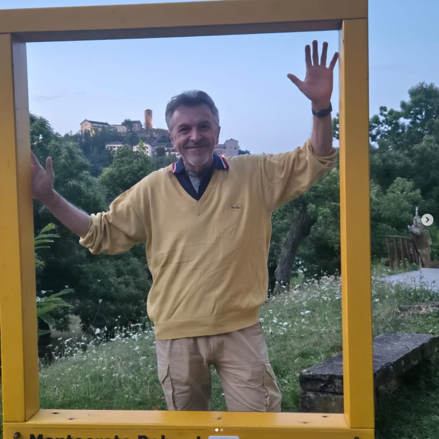 Patrizio Oca in piedi all'interno di una cornice, con il borgo dipinto sullo sfondo